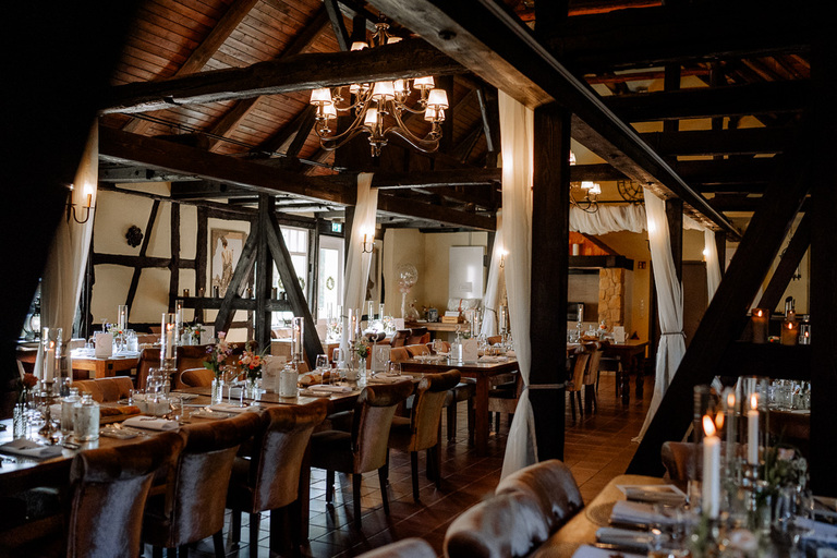 Blick in den rustikalen Hochzeitsfestsaal der Moormühle mit Holzbalken und romantischer Beleuchtung
