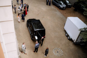 Gäste stehen vor dem Schloss Eldingen, während ein elegantes Hochzeitsauto bereitsteht.