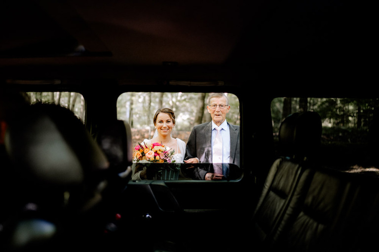 Die Braut und ihr Onkel werden durch das Fenster des Hochzeitsautos fotografiert.