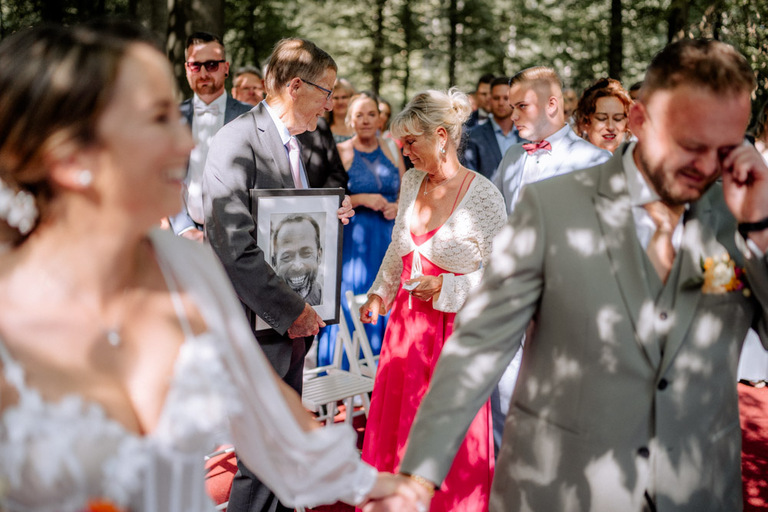 Familienmitglied hält ein gerahmtes Foto eines verstorbenen Angehörigen während der Hochzeit.