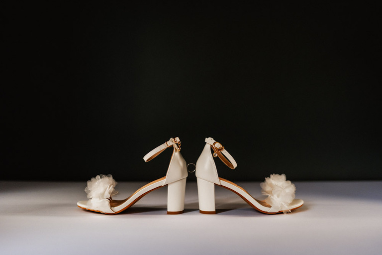 Weiße Brautschuhe mit floralen Details vor einem dunklen Hintergrund
