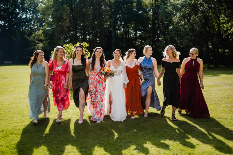 Die Braut mit ihren Brautjungfern in eleganten Kleidern, lachend und Hand in Hand auf einer Wiese des Schlosses Eldingen.