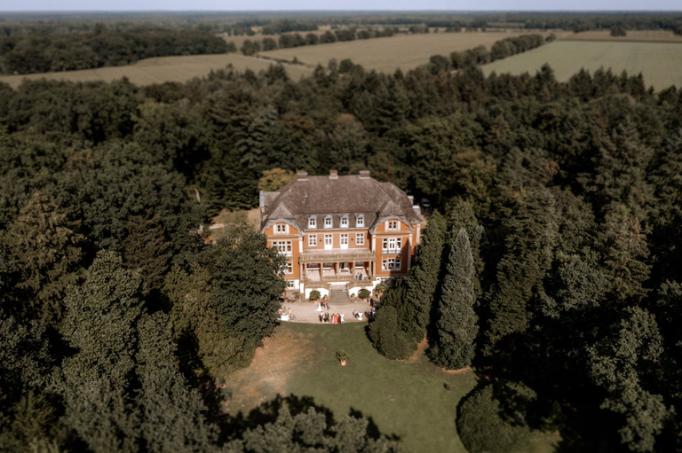 Luftaufnahme von Schloss Eldingen, umgeben von dichten Wäldern und grünen Feldern.