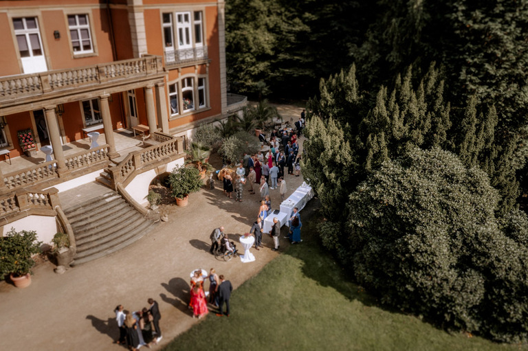 Gäste bei einem Hochzeitsempfang auf der Terrasse von Schloss Eldingen, mit Blick auf die wunderschöne Fassade.