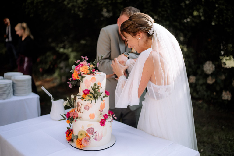 Eine detailreich dekorierte Hochzeitstorte mit Blumen in kräftigen Farben.