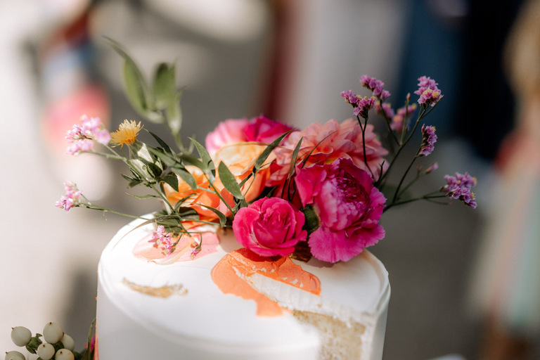 Nahaufnahme einer Hochzeitstorte mit frischen Blumen und pastellfarbenen Akzenten.