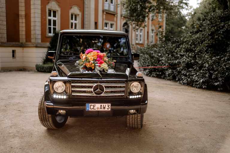 Schwarzes Hochzeitsauto mit bunter Blumendekoration vor Schloss Eldingen.