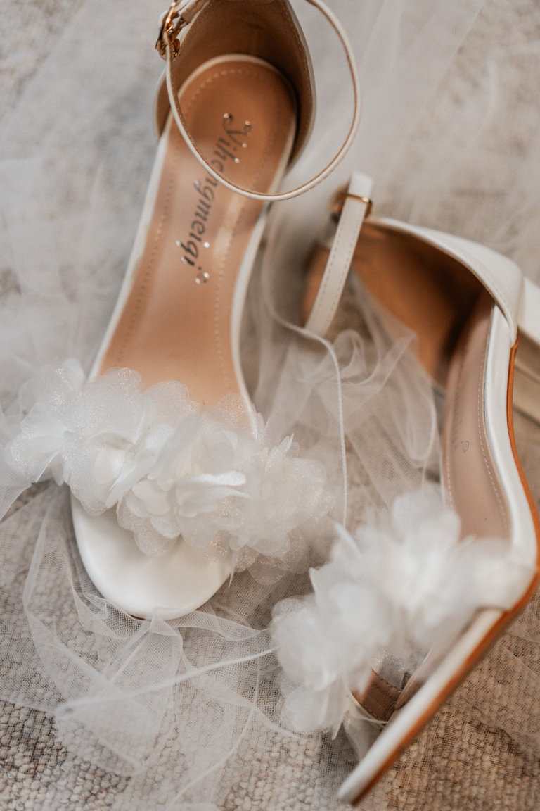 Nahaufnahme von weißen Brautschuhen mit floralen Details und einem Hauch von Tüll.