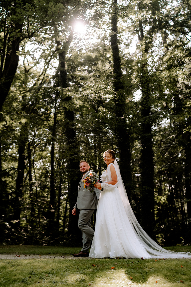 Braut und Bräutigam im Sonnenschein, umgeben von Bäumen im Schlosspark von Eldingen