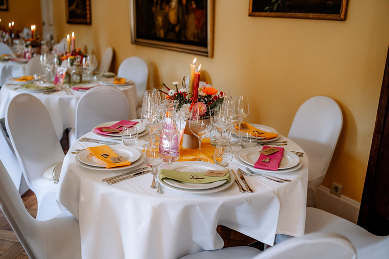 Stilvoll gedeckte Hochzeitstafeln mit warmen Farben in einem gelben Saal von Schloss Eldingen.